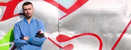 The graffiti artist with spray can poses against the background of a colorful painted wall. Street art concept photo