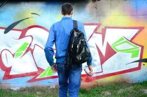 A young graffiti artist with a black bag looks at the wall with his graffiti on a wall. Street art concept photo