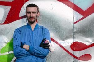 The graffiti artist with spray can poses against the background of a colorful painted wall. Street art concept photo