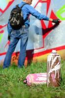 A few used paint cans against the background of the space with the wall on which the young guy draws a large graffiti drawing. Modern art of drawing walls in graffiti photo