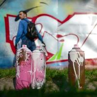 A few used paint cans against the background of the space with the wall on which the young guy draws a large graffiti drawing. Modern art of drawing walls in graffiti photo