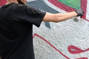 A young hooligan paints graffiti on a concrete wall. Illegal vandalism concept. Street art photo