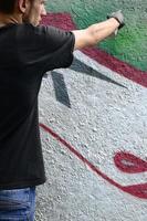 A young hooligan paints graffiti on a concrete wall. Illegal vandalism concept. Street art photo