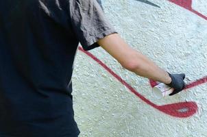 A young hooligan paints graffiti on a concrete wall. Illegal vandalism concept. Street art photo