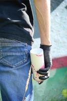 A young hooligan with a spray can stands against a concrete wall with graffiti paintings. Illegal vandalism concept. Street art photo