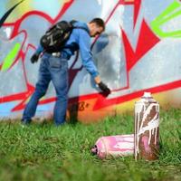 A few used paint cans against the background of the space with the wall on which the young guy draws a large graffiti drawing. Modern art of drawing walls in graffiti photo