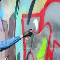 A hand with a spray can that draws a new graffiti on the wall. Photo of the process of drawing a graffiti on a metal wall. The concept of street art and illegal vandalism