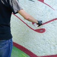 A young hooligan paints graffiti on a concrete wall. Illegal vandalism concept. Street art photo