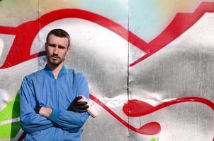 The graffiti artist with spray can poses against the background of a colorful painted wall. Street art concept photo