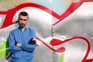 The graffiti artist with spray can poses against the background of a colorful painted wall. Street art concept photo