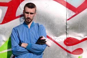 The graffiti artist with spray can poses against the background of a colorful painted wall. Street art concept photo