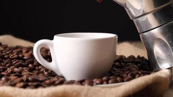 Pouring coffee from moka in espresso cup with jute and coffee beans background video