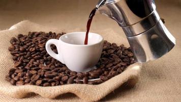 Pouring coffee from moka in espresso cup with jute and coffee beans background video