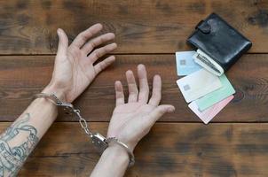 Cuffed hands of tattooed criminal suspect of carding and fake credit cards with cash in purse as evidence for investigation photo