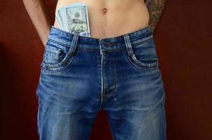 The body of a guy in blue jeans with a lot of dollar bills, visible from under the clothes photo