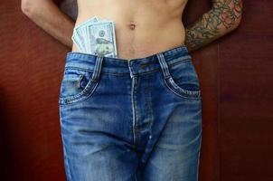 The body of a guy in blue jeans with a lot of dollar bills, visible from under the clothes photo