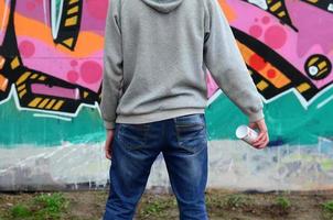 A young graffiti artist in a gray hoodie looks at the wall with photo