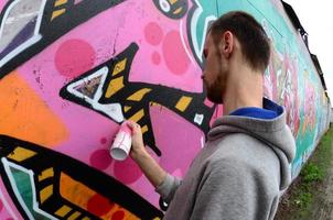 un joven con una sudadera con capucha gris pinta graffiti en rosa y verde c foto