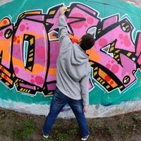 A young guy in a gray hoodie paints graffiti in pink and green c photo