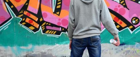 A young graffiti artist in a gray hoodie looks at the wall with photo