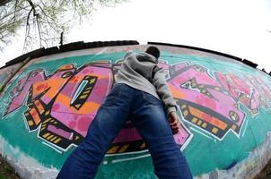 A young guy in a gray hoodie paints graffiti in pink and green c photo