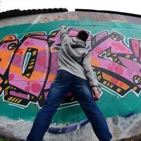 A young guy in a gray hoodie paints graffiti in pink and green c photo