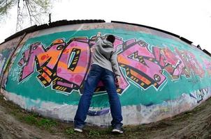 A young guy in a gray hoodie paints graffiti in pink and green c photo