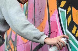 un joven con una sudadera con capucha gris pinta graffiti en rosa y verde c foto