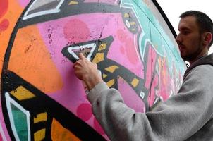 A young guy in a gray hoodie paints graffiti in pink and green c photo