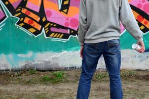 A young graffiti artist in a gray hoodie looks at the wall with photo