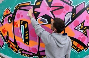 A young guy in a gray hoodie paints graffiti in pink and green c photo