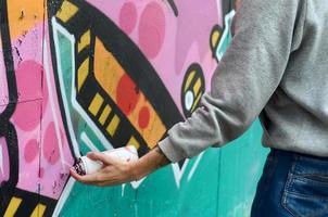 Hand of a young guy in a gray hoodie paints graffiti in pink and photo