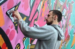 A young guy in a gray hoodie paints graffiti in pink and green c photo