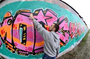 A young guy in a gray hoodie paints graffiti in pink and green c photo