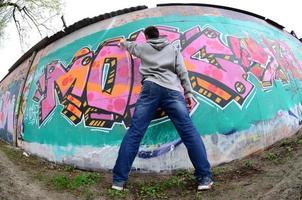 A young guy in a gray hoodie paints graffiti in pink and green c photo