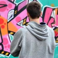 A young graffiti artist in a gray hoodie looks at the wall with photo