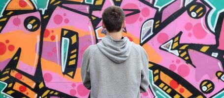 A young graffiti artist in a gray hoodie looks at the wall with photo