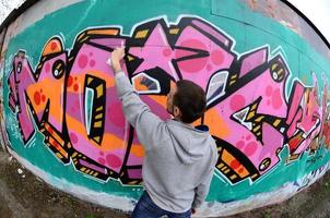 A young guy in a gray hoodie paints graffiti in pink and green c photo