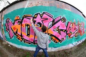 A young guy in a gray hoodie paints graffiti in pink and green c photo