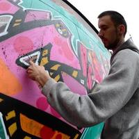 A young guy in a gray hoodie paints graffiti in pink and green c photo