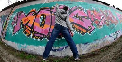 A young guy in a gray hoodie paints graffiti in pink and green c photo