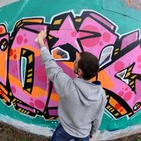 A young guy in a gray hoodie paints graffiti in pink and green c photo