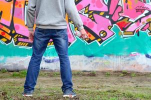 A young graffiti artist in a gray hoodie looks at the wall with photo