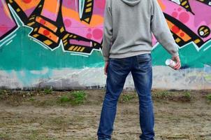 A young graffiti artist in a gray hoodie looks at the wall with photo