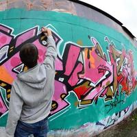 A young guy in a gray hoodie paints graffiti in pink and green c photo