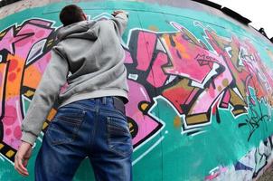 un joven con una sudadera con capucha gris pinta graffiti en rosa y verde c foto