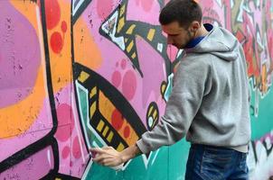 A young guy in a gray hoodie paints graffiti in pink and green c photo