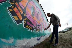 A young guy in a gray hoodie paints graffiti in pink and green c photo