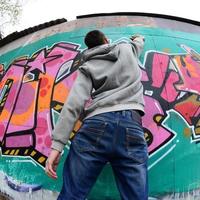 A young guy in a gray hoodie paints graffiti in pink and green c photo