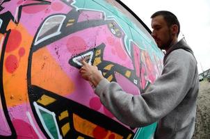 A young guy in a gray hoodie paints graffiti in pink and green c photo